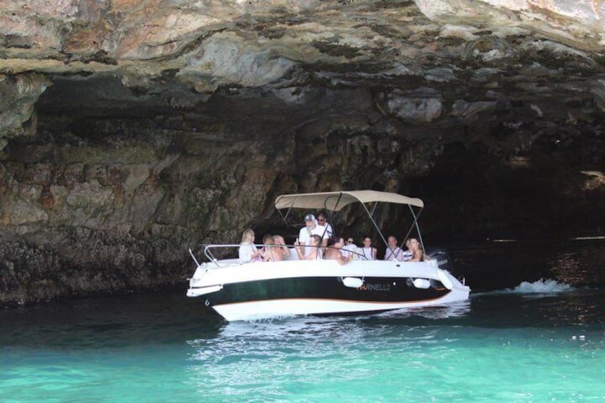 Ein Boot mit Passagieren fährt durch eine klare, blaue Wasserstraße unter dem Felseneingang einer Höhle. 3
