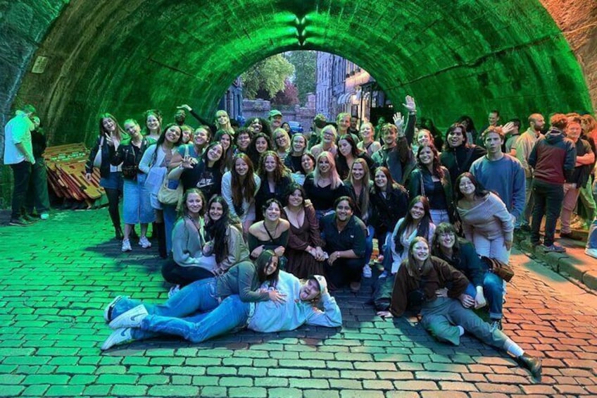 A group of people posing under a green-lit archway in a city setting. 2