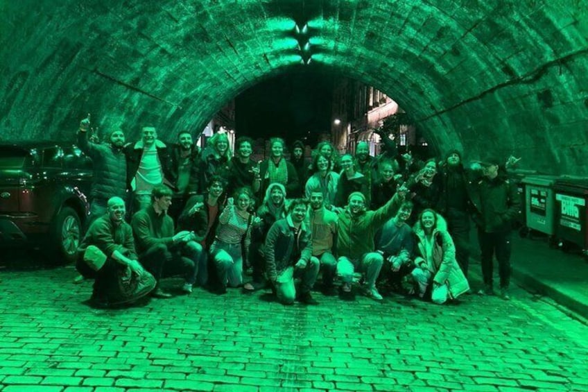 A group of people posing in a tunnel with a brick floor and a greenish hue. 4