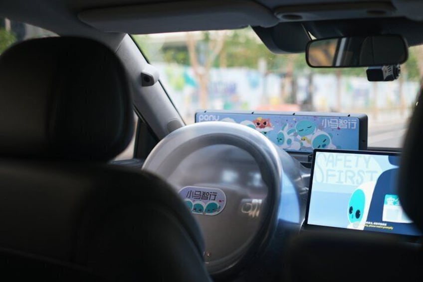 A car's interior with a steering wheel, dashboard, and two screens displaying safety messages. 1