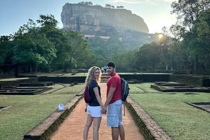 A couple standing in a garden with a large rock formation in the background. 3