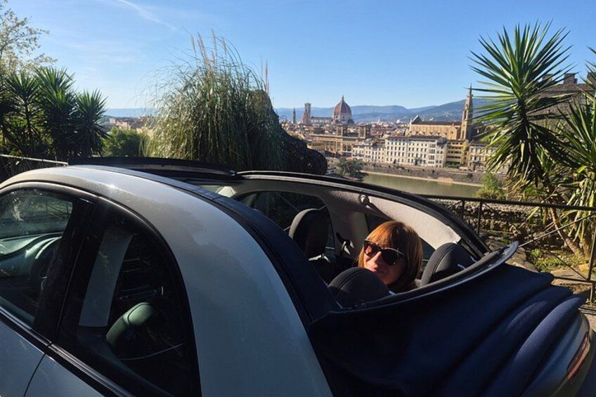 A convertible car parked on a balcony overlooking a cityscape with a prominent dome-shaped building in the background. 5