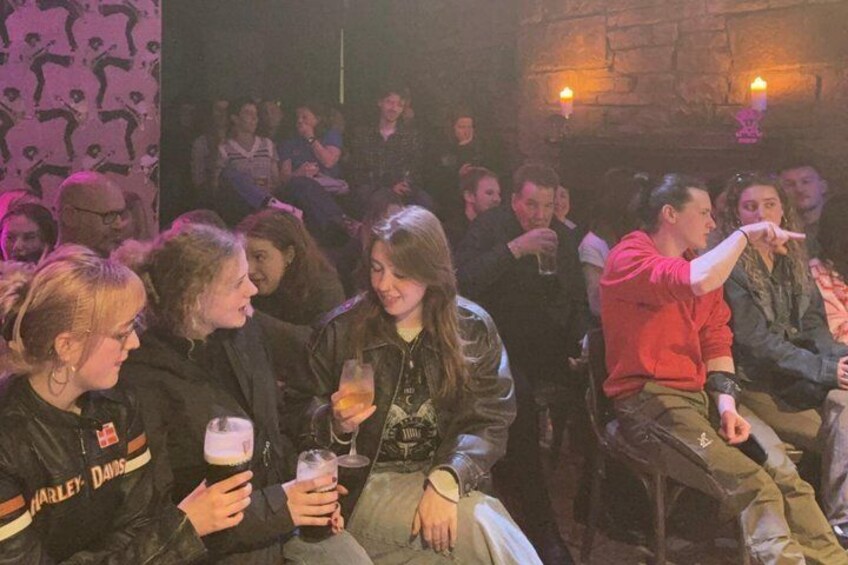 A group of people seated in a dimly lit room, some holding drinks. 4