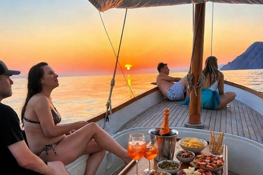 Solnedgang fra en båd, hvor folk slapper af ved et bord med mad og drikke. 1