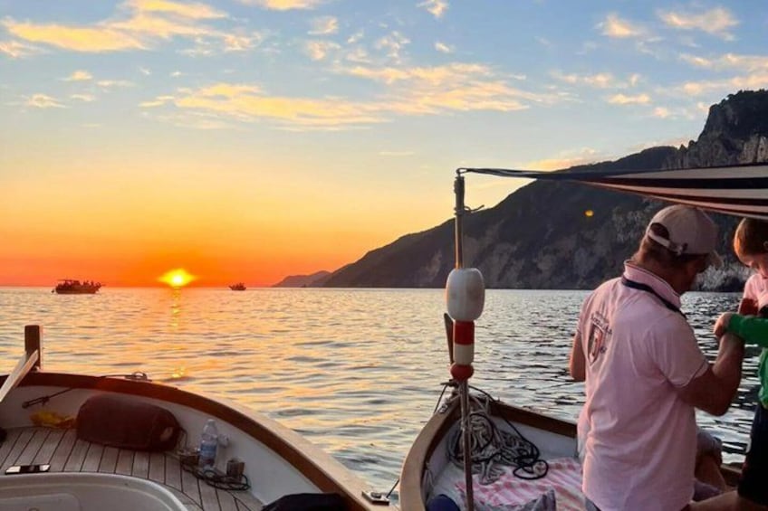 A sunset over a calm sea with boats, a rocky coastline, and a person standing on a boat. 2