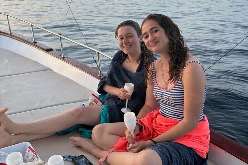 Two people sitting on a boat, holding drinks, with water in the background. 2