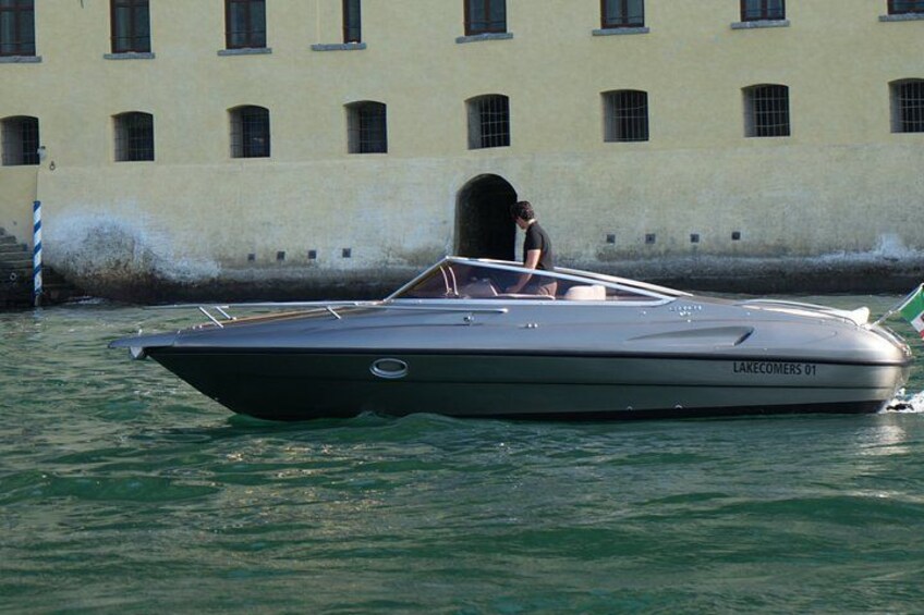 Un bateau à moteur rapide, baptisé « LAKECOMERS 01 », navigue sur l’eau, avec un bâtiment visible en arrière-plan. 2