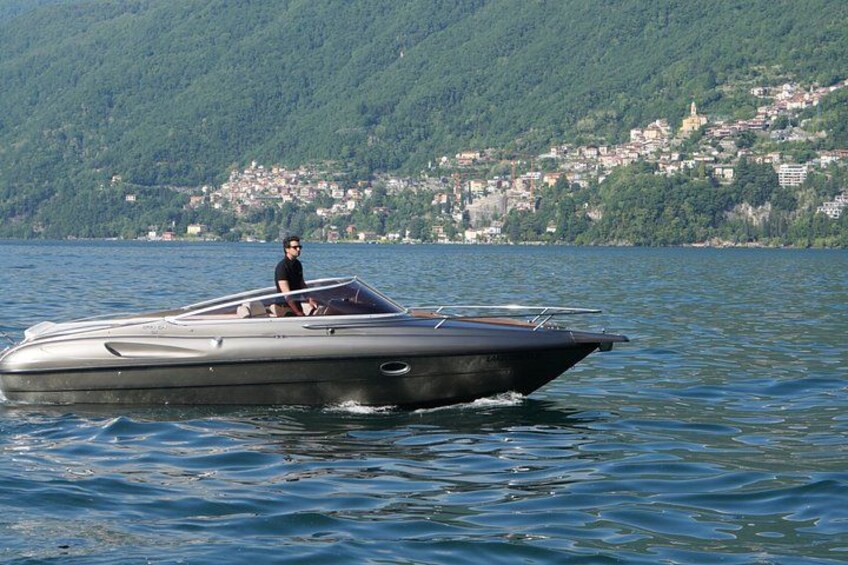 Un bateau à moteur sur une étendue d’eau calme, avec une personne à bord. Au fond, on aperçoit un paysage vallonné avec une ville. 4