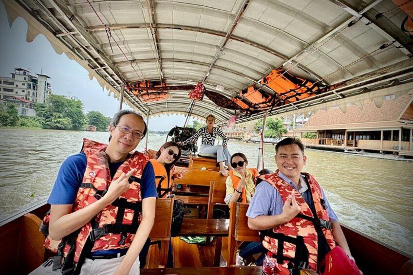 A boat with people wearing life jackets, a covered roof, and a river with buildings in the background. 2