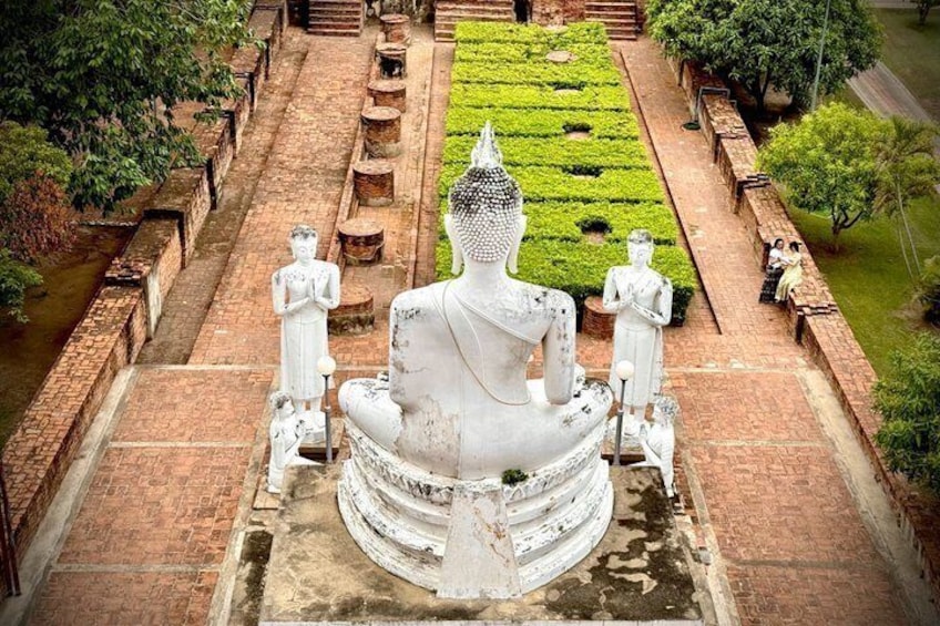 A large white stupa surrounded by smaller statues, set in a brick courtyard with a green garden in the background. 3