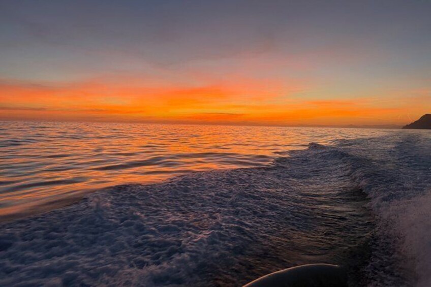 Un coucher de soleil sur l’océan, avec des vagues, une terre lointaine et un bateau. 5