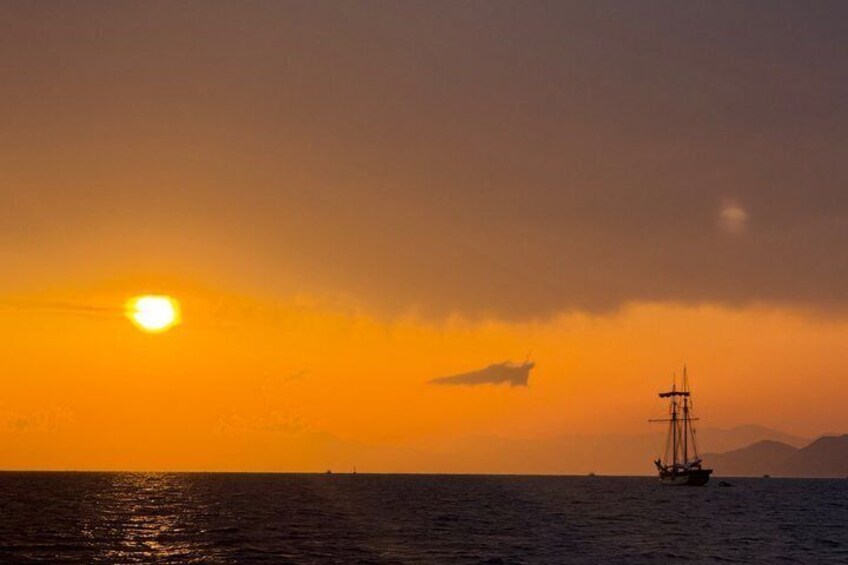 Un coucher de soleil sur l’océan, avec un voilier et un navire à l’horizon. 3