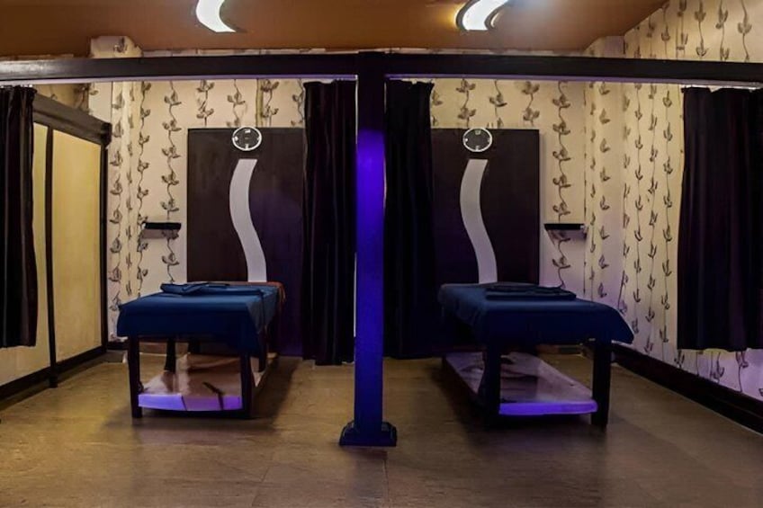 Een kamer met twee massagetafels, een centrale pilaar en behang met een patroon. 3