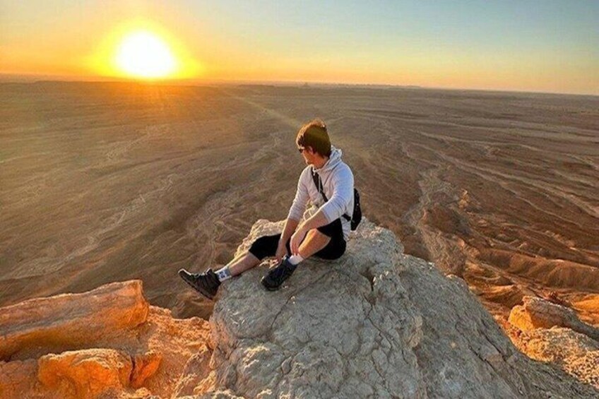 A person sitting on a rock with a vast desert landscape and a setting sun in the background. 5