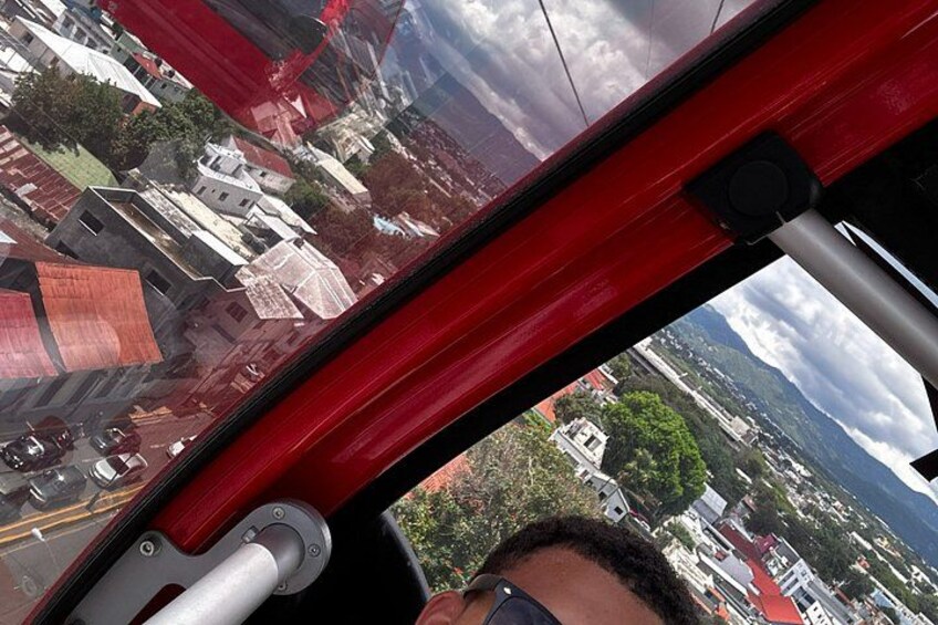 Une vue depuis la fenêtre d’un hélicoptère, montrant une structure rouge, un bâtiment blanc et un paysage montagneux. 3
