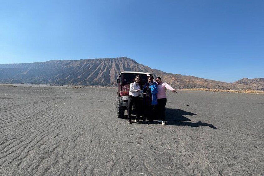 Un groupe de personnes posant à côté d’un véhicule dans un paysage désertique, avec des montagnes en arrière-plan. 3