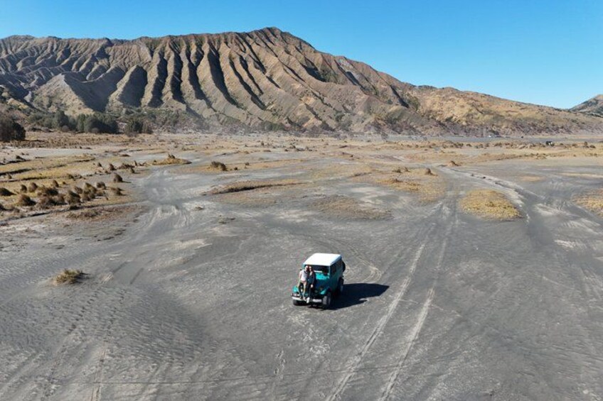A vehicle on a dirt road in a barren landscape with mountains in the background. 2
