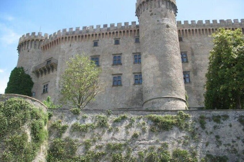 A historic stone castle with a large central tower, a crenellated wall, and a well-maintained garden. 5