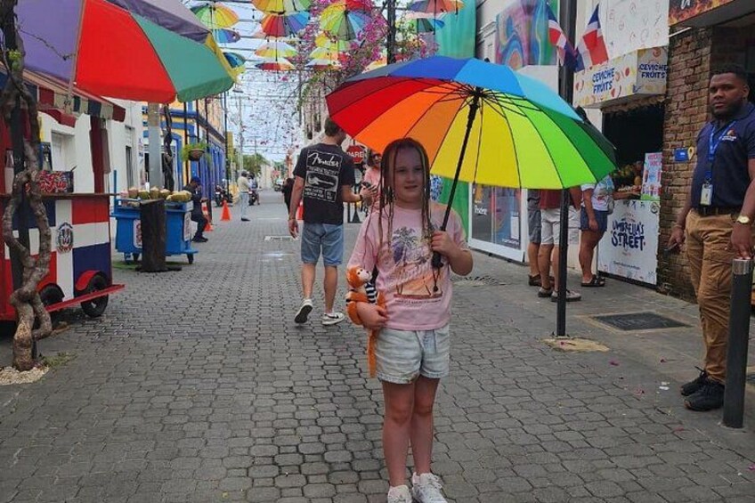 A street with colorful umbrellas, a food cart, and a person holding a drink. 4