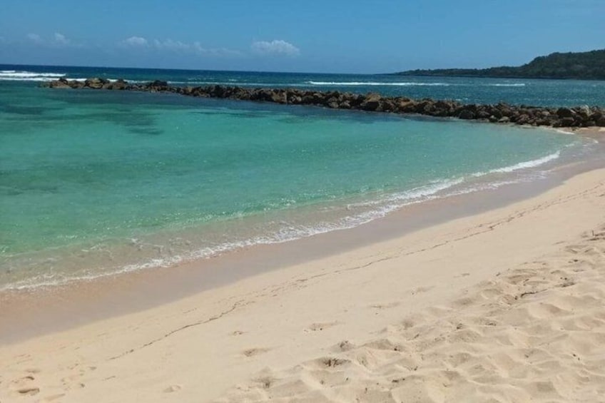 A sandy beach with clear turquoise water and a rocky breakwater. 3