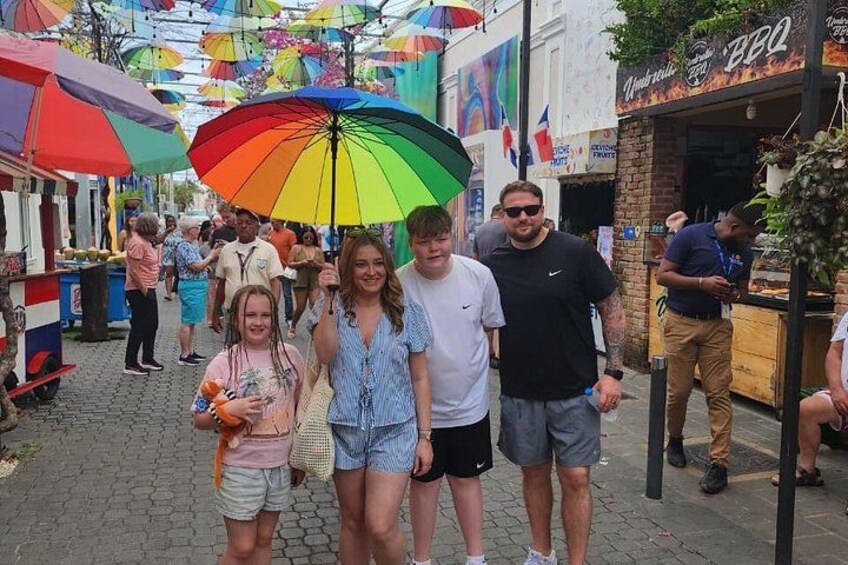 A street market with people walking, colorful umbrellas, and food stalls. 2