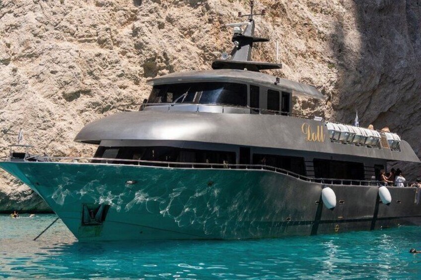 A large boat with 'Loll' written on its side, docked near a rocky cliff. 1