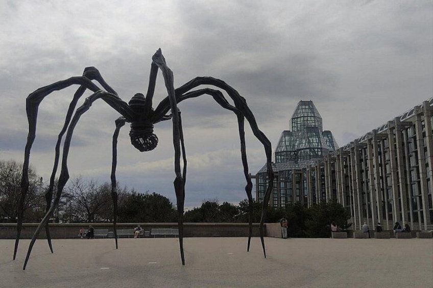 A large metal sculpture of a spider in an open plaza with a modern building in the background. 3