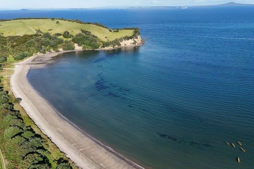 A coastal landscape with a sandy beach, a curved shoreline, and a clear blue sea. 4