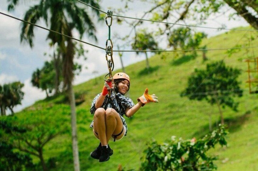 A person zip-lining with a helmet and gloves, surrounded by greenery and hills. 1