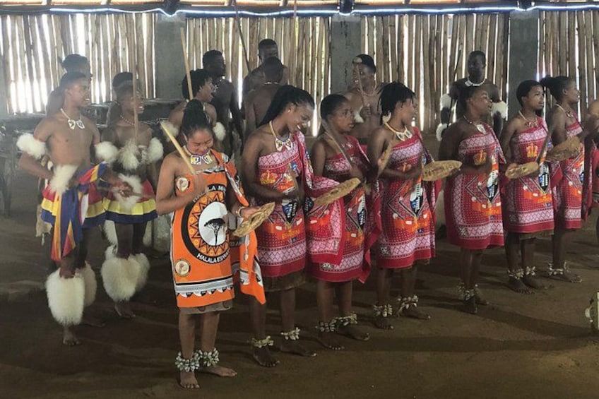 Un grupo de personas con vestimenta tradicional, algunas sosteniendo abanicos, de pie en fila frente a un telón de fondo. 1