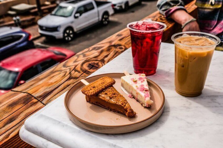 Un tavolo di legno con un piatto di cibo, una bevanda rossa e un bicchiere di caffè freddo. 1