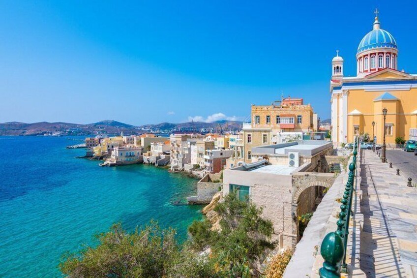A coastal town with buildings, a clear blue sea, and a prominent church with a blue dome. 1
