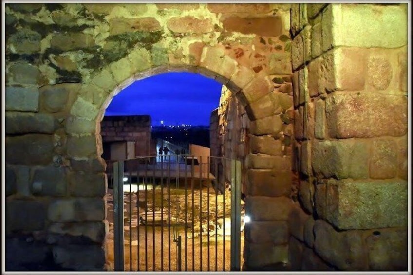 An arched stone gateway leading to a courtyard with a metal gate, surrounded by stone walls. 2