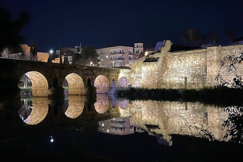 A stone bridge with arches reflecting in the water at night. 4