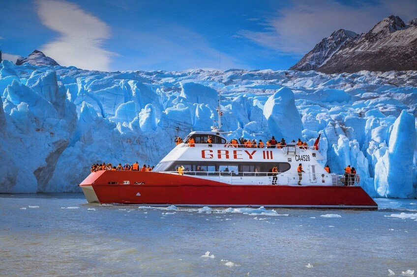 A tour boat named 'GREY III' with passengers wearing orange life jackets, navigating near a glacier. 5