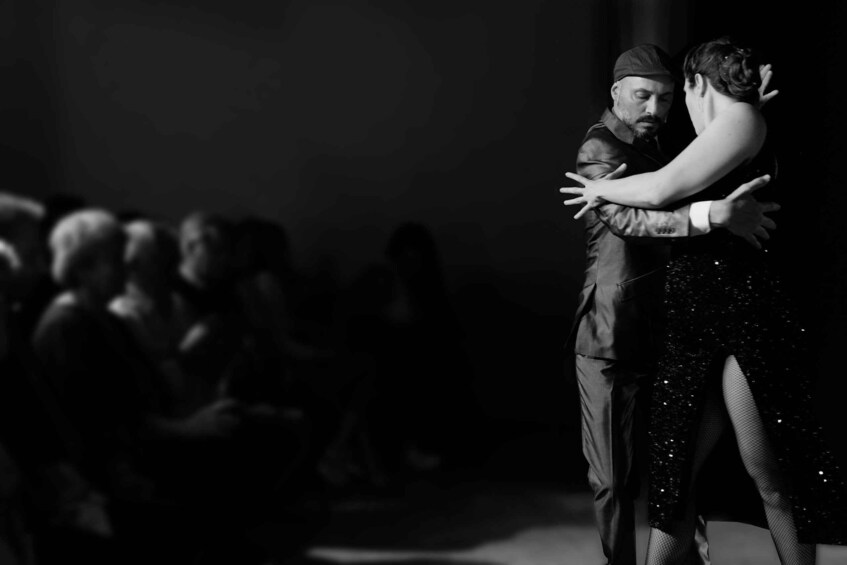 Una pareja bailando en un escenario, con un público en el fondo. 5