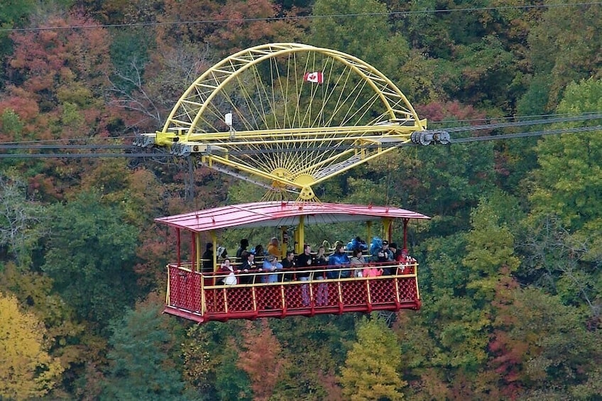 A cable car system with a red car suspended by cables, a large yellow cable wheel, and a forested background. 4