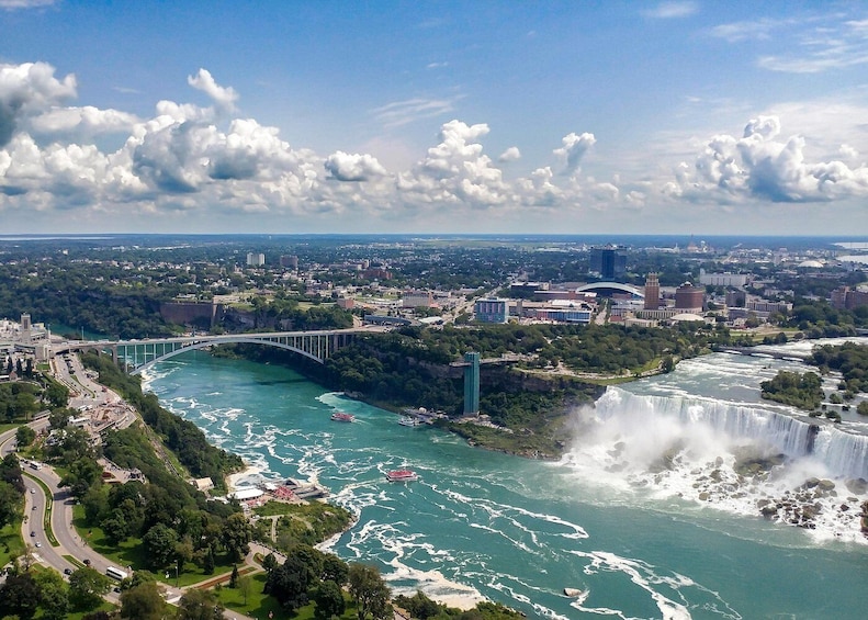 A river with a waterfall, a bridge, and a cityscape with buildings and greenery. 2