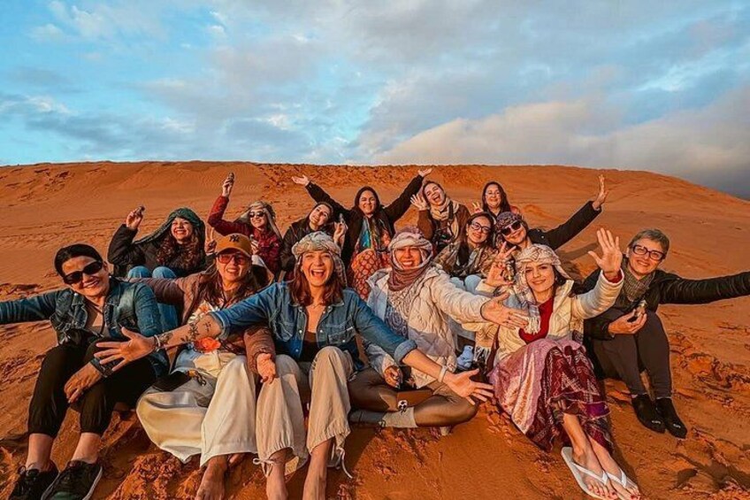 A group of people sitting on the sand dunes with their arms outstretched. 1