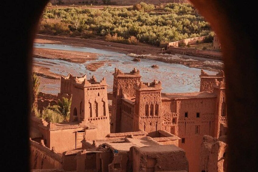 A desert landscape with a traditional mud-brick building complex, a river, and sparse vegetation. 4