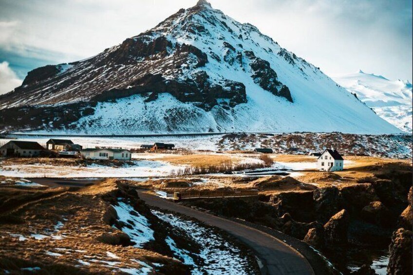 A snow-covered mountain, a small white house, and a road leading to a bridge. 4