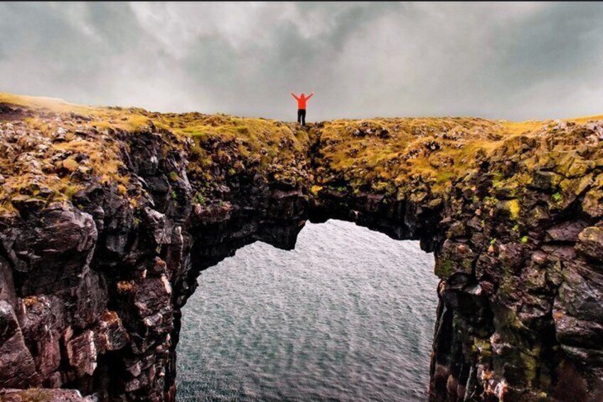 A person standing on a rocky ledge with arms raised, overlooking a large body of water. 5