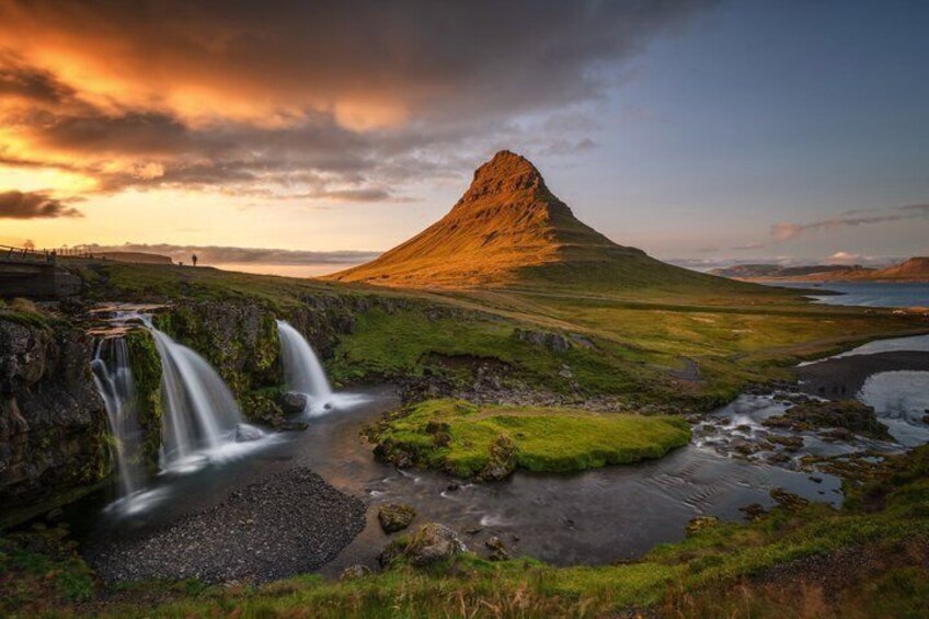 A waterfall, grassy landscape, and a mountain. 1