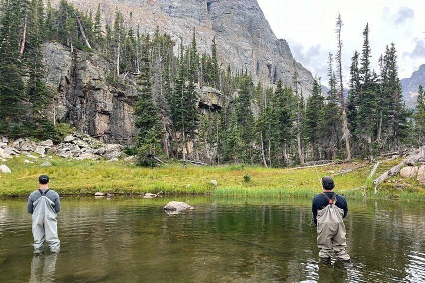 Two people wading in a river surrounded by trees and mountains. 4