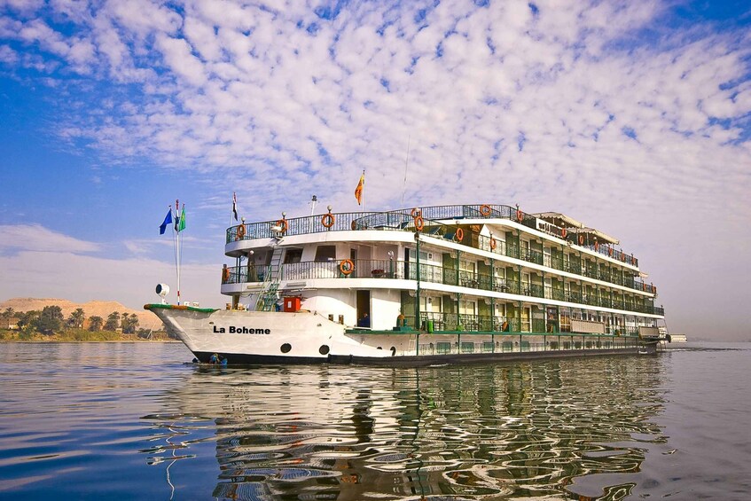 A large, multi-deck river cruise ship named 'La Bohème' with lifeboats and flags, docked at a calm river with a clear sky. 4