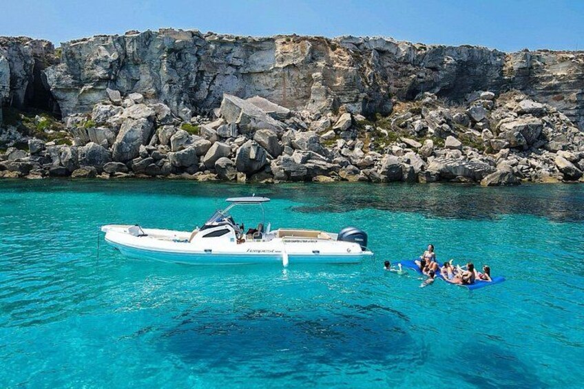 A boat on clear turquoise water with a rocky shoreline in the background. 3