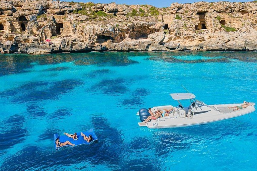 A boat with people on a clear blue sea, rocky cliffs in the background. 4