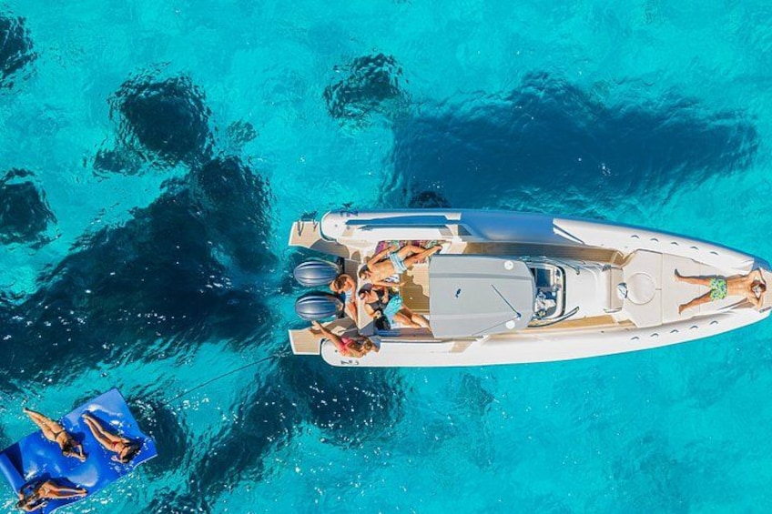 A white boat with people on board, anchored in turquoise water with visible rocks. 2