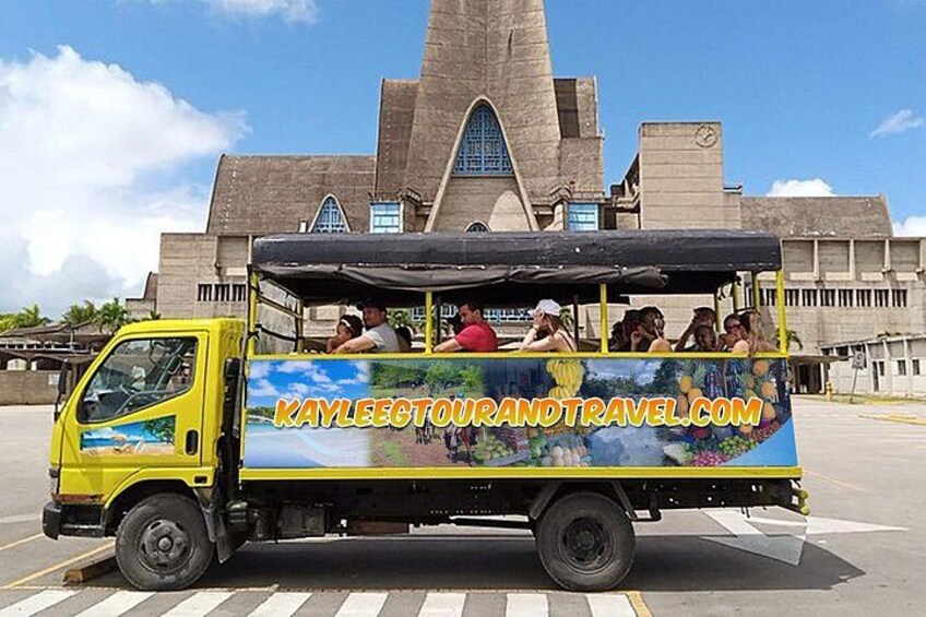 A yellow tour bus with passengers, parked in front of a large building with a distinctive tower. 2