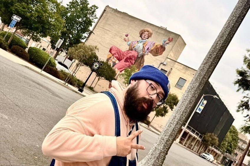 Una persona con camisa rosa y gorro azul, de pie en una calle con un mural de un niño al fondo. 2
